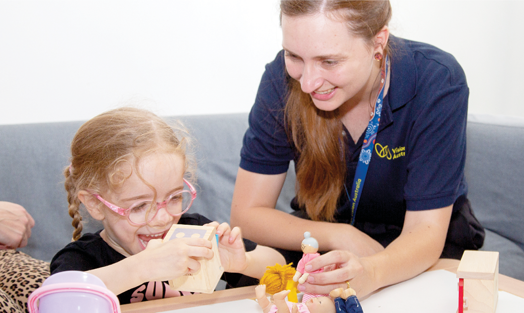 Young girl and Vision Australia orientation mobility specialist are smiling and playing with toys