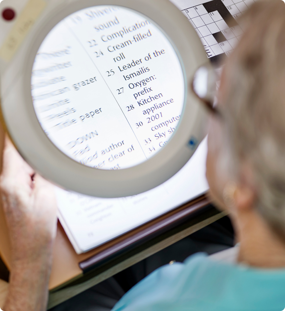 An older lady uses a magnifier to read the crossword