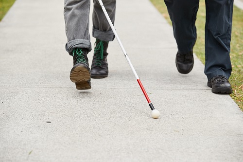 Two people walk along a footpath, one using a white cane