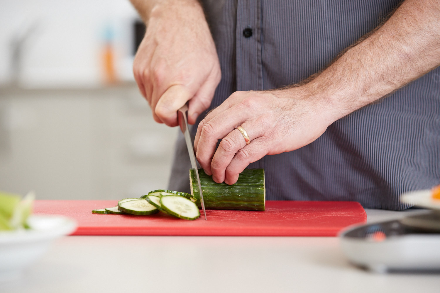 "A man cuts a cucumber on a red chopping board"