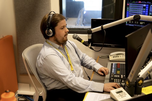 "A man sits in a radio studio with a microphone near his mouth"
