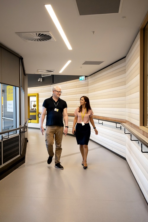 Two colleagues, one male and one female, walk down a corridor