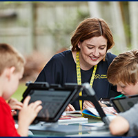 Vision Australia staff member supports a group of chidren who are using tablet devices.
