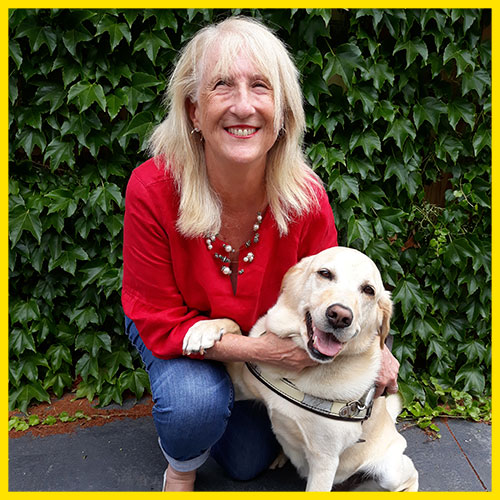 Di is kneeling alongside her dog guide, and the dog is resting his paw on her arm