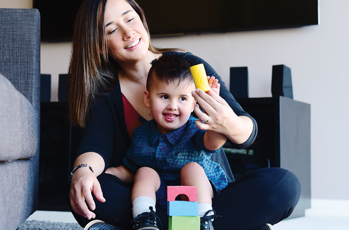 Gabe is smiling and sitting with his mum playing blocks