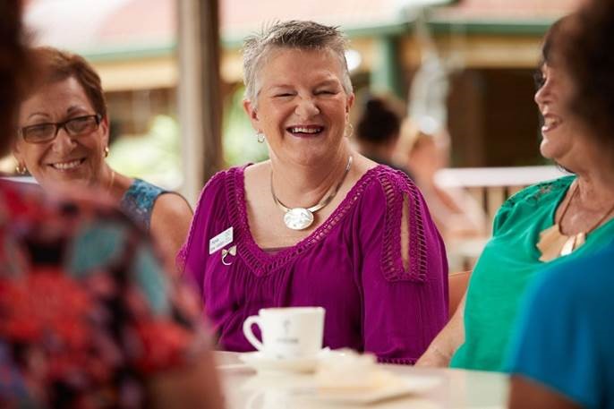 A woman happily smiling and chatting to other woman at a table