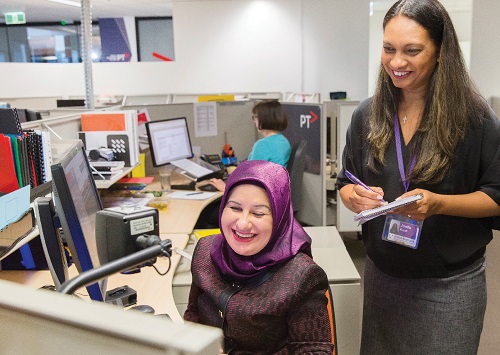 A woman sits a computer as another woman looks over her shoulder