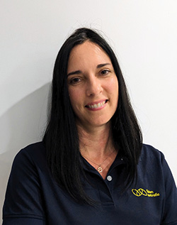 A woman with long dark hair and wearing a navy Vision Australia polo shirt smiles at the camera