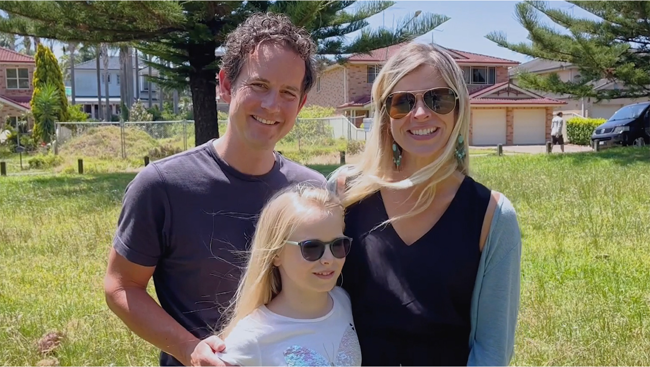 Gemma, a nine-year-old girl with long blonde hair, stands outside in the sun with her parents. All of them are smiling