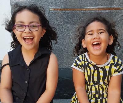 The picture shows Paisley and Olive, two small girls, sitting next to each other with big smiles on their faces.
