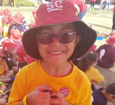Paisley, aged 5, is dressed in her sports uniform and is wearing a hat and sunglasse. The photo was taken at the cross country event.