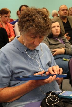 Coral using a braille display Photo of Coral sitting in audience using a braille display