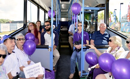 Group of people in a bus holding balloons and signs for White Cane Day