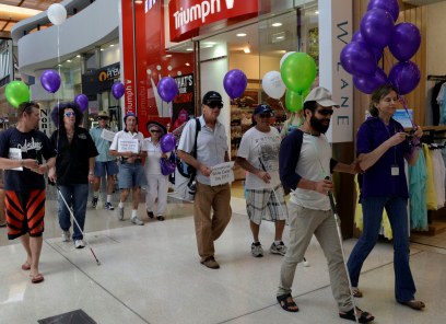 Group of people walking through a Gold Coast shopping centre with balloons and signs for White Cane Day
