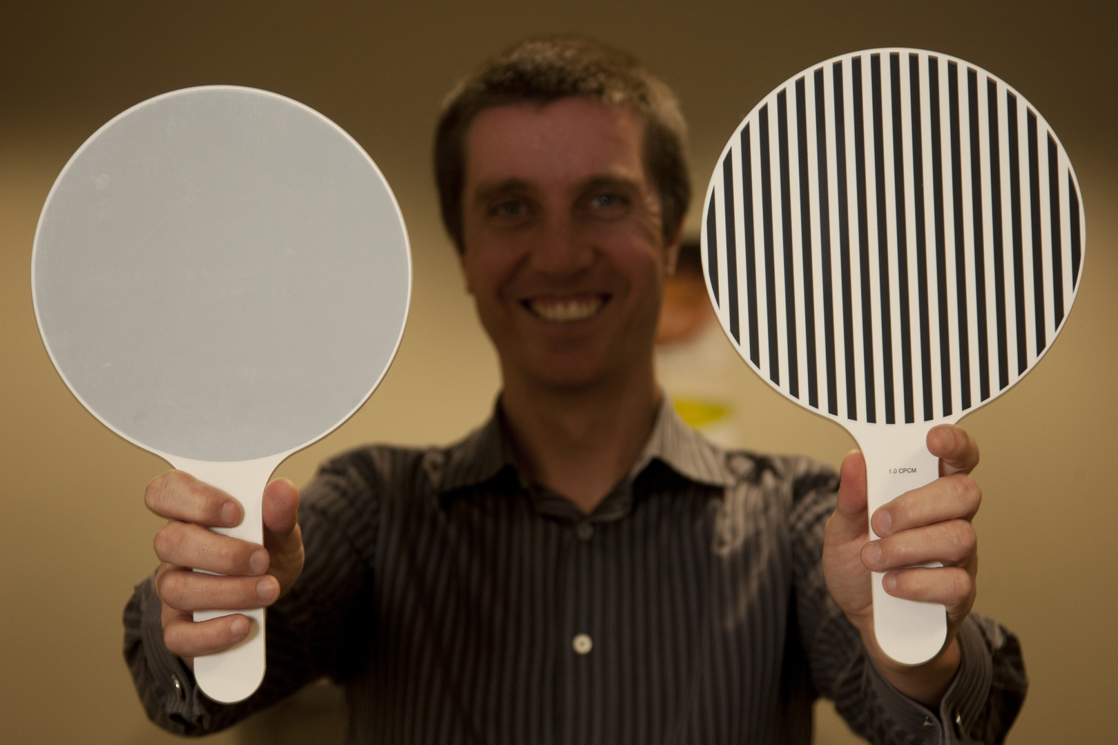 Man holds up two paddles, one is striped and the other is grey.