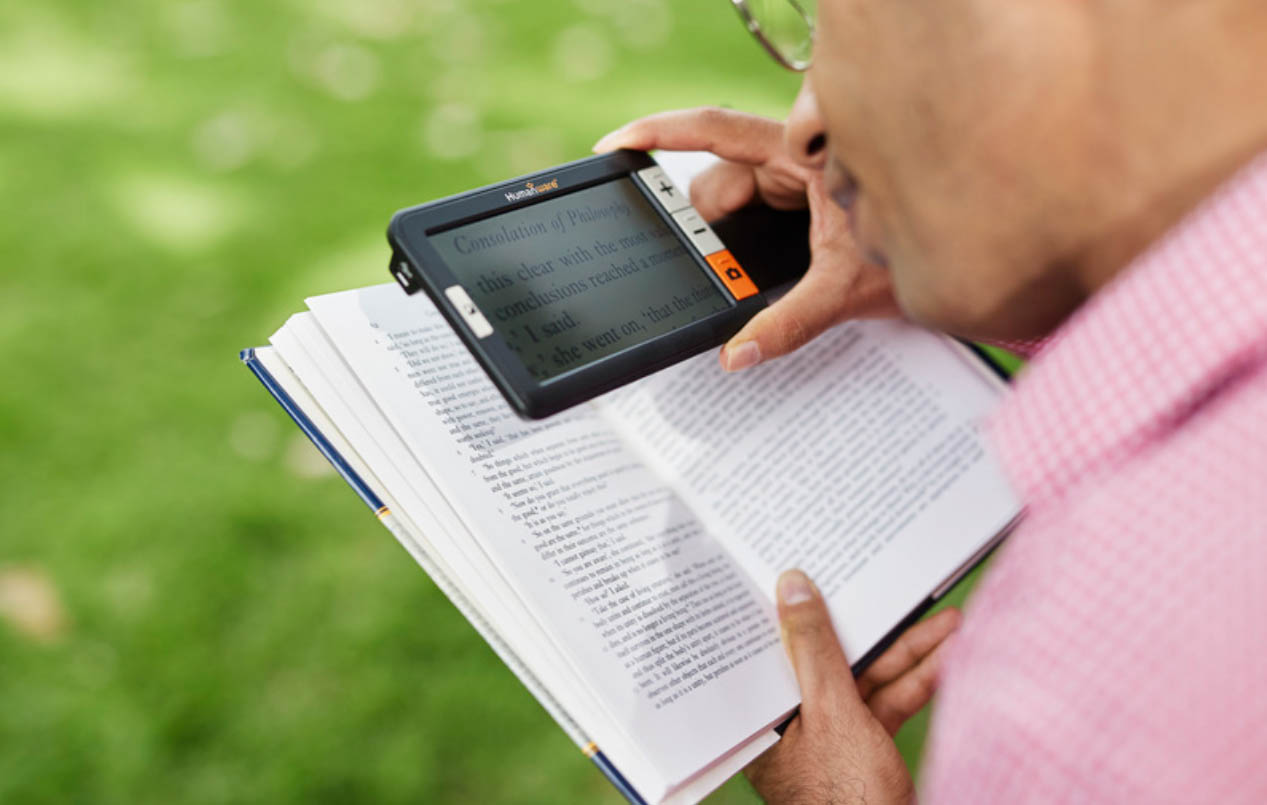 A man using a handheld magnified to read text on a book.
