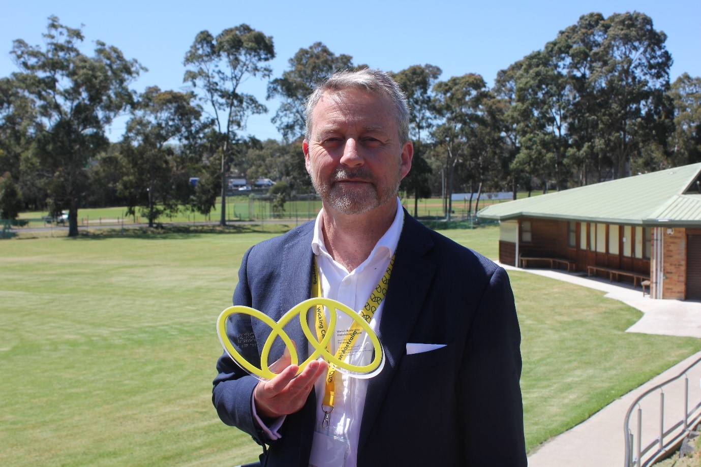 " VA Award winner Tim, holding his award which takes the shape of the VA logo of 3 yellow ovals linked together"
