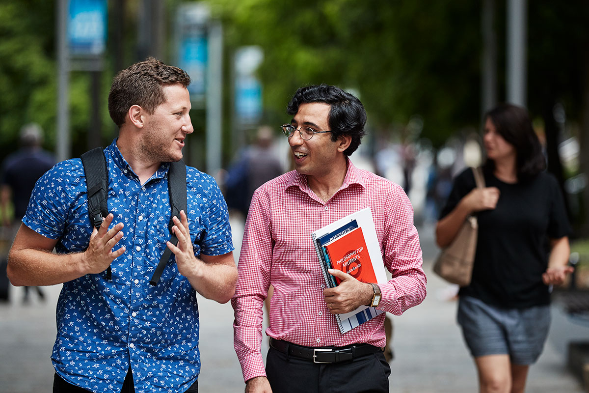 Two students are chatting as they walk, one holding books