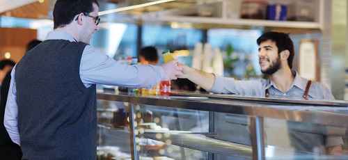 A man in a cafeteria reaches over a counter to buy a drink