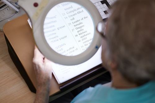 An older women uses a magnifier to complete a crossword