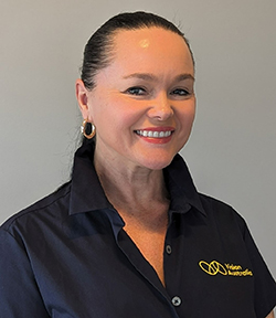 A woman with a black ponytail and wearing a navy Vision Australia polo shirt smiles at the camera
