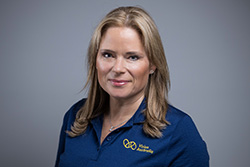 A woman with blonde hair and wearing a navy Vision Australia polo shirt smiles at the camera