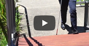 Video play icon. A man using a white cane and stepping up stairs