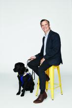 Chris Edwards sitting on a yellow chair next to Odie his Seeing Eye Dog