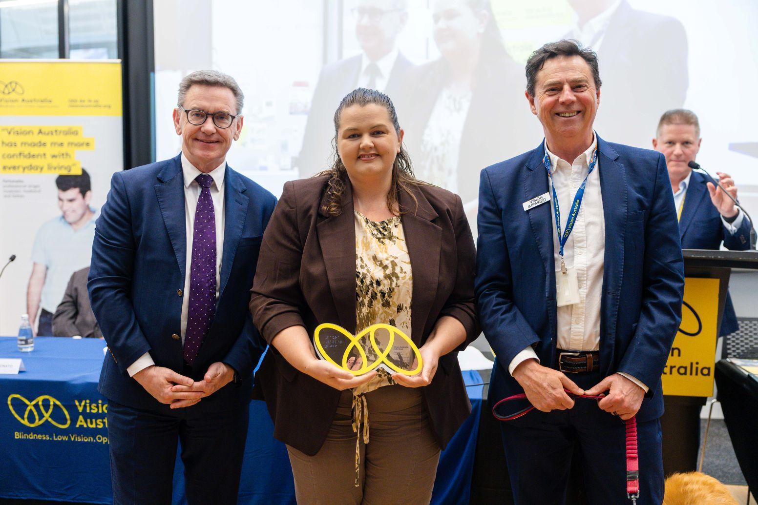 Laura Walker holds her Vision Australia Award and stands next to Vision Australia CEO David Williamson and Chair Mark Grey