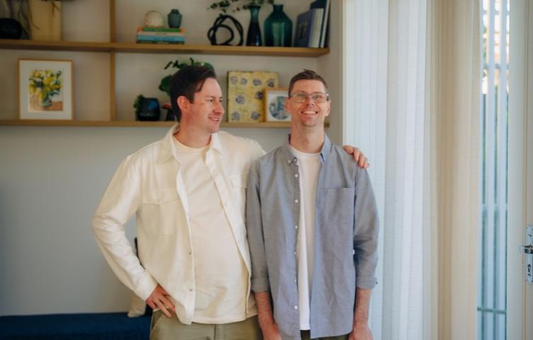 A man stands smiling at the camera, his support worker beside him.