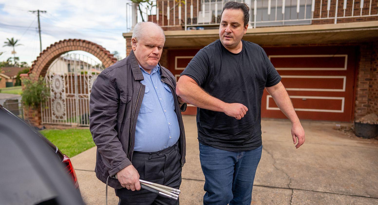 A rideshare driver guides a passenger holding a white cane to a vehicle