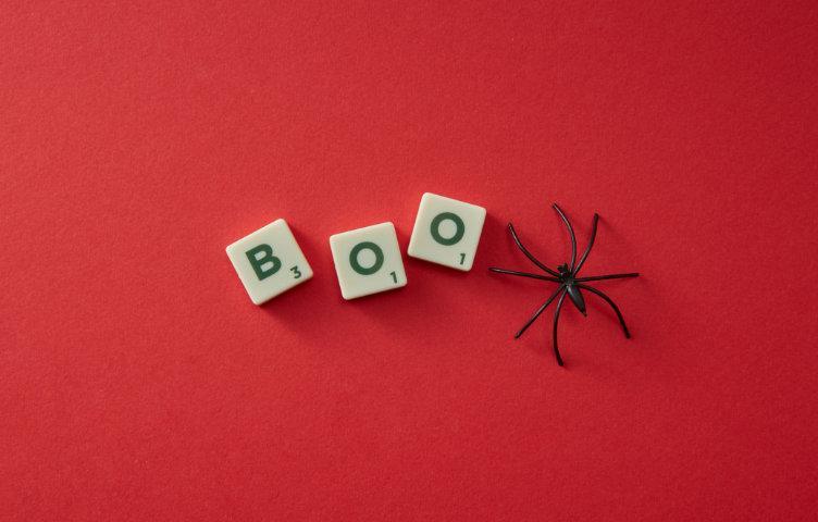 A red background with 3 tiles that spell the word Boo and a black spider beside them.