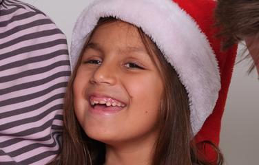 A little girl with brown hair wearing a Santa hat.