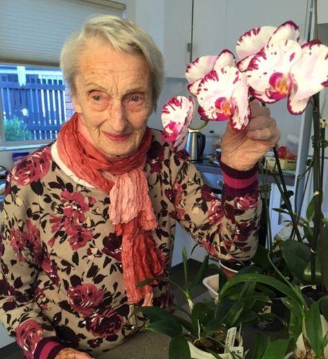 An older lady standing with some orchids.