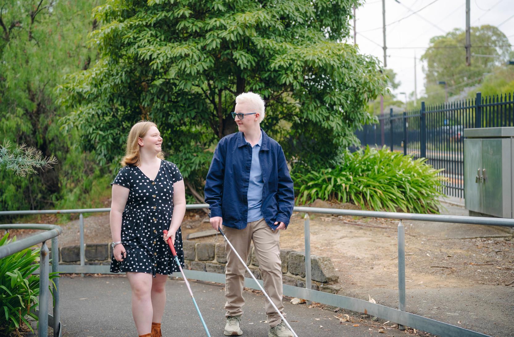 A man and a woman are walking together, both of them holding white canes.